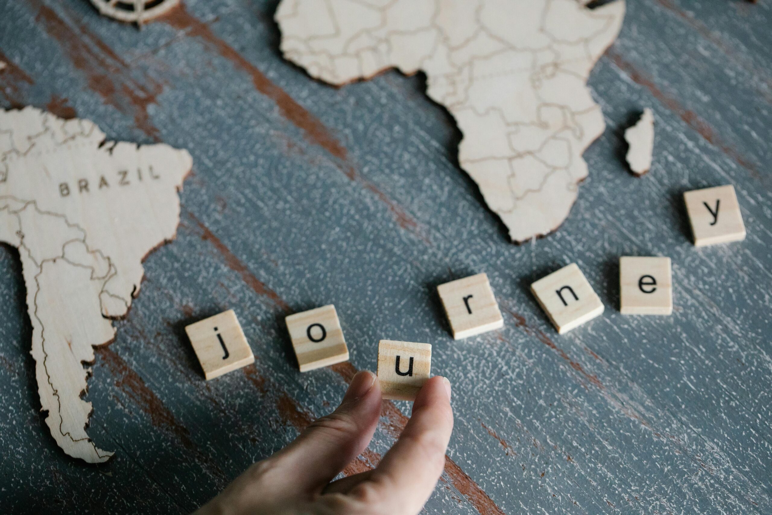 Wooden blocks spelling 'journey' with map cutouts of Brazil and Africa on a table.